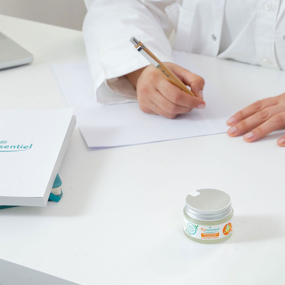 Persoon schrijft. Pot: Puressentiel, Spieren & Gewrichten, verzachtende balsem. 14 essentiële oliën.