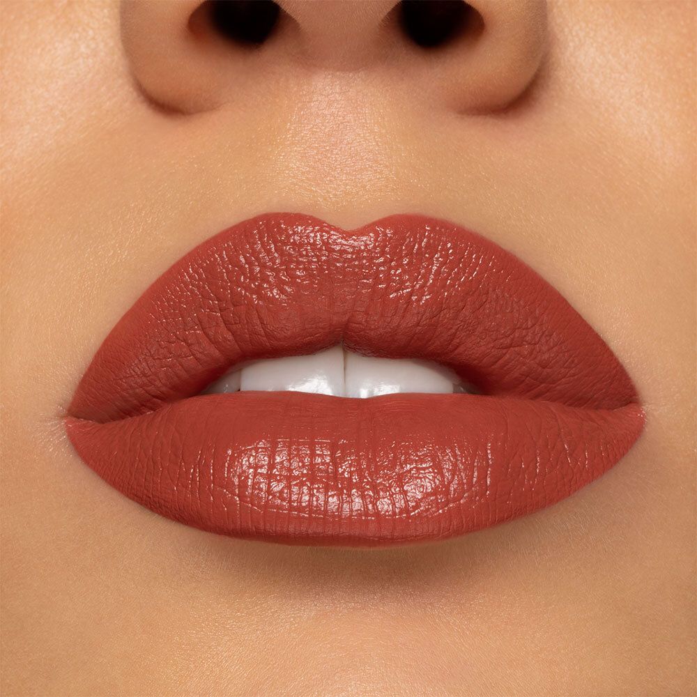 Close-up van lippen bedekt met semi-matte perzikroze lipstick. Huidtint zichtbaar. Glanzende finish.