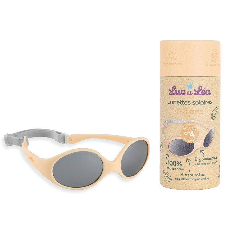 Beige zonnebril met grijze glazen en grijze band. Daarnaast de verpakking. Opschrift: Luc & Léa, zonnebril 1-3 jaar.