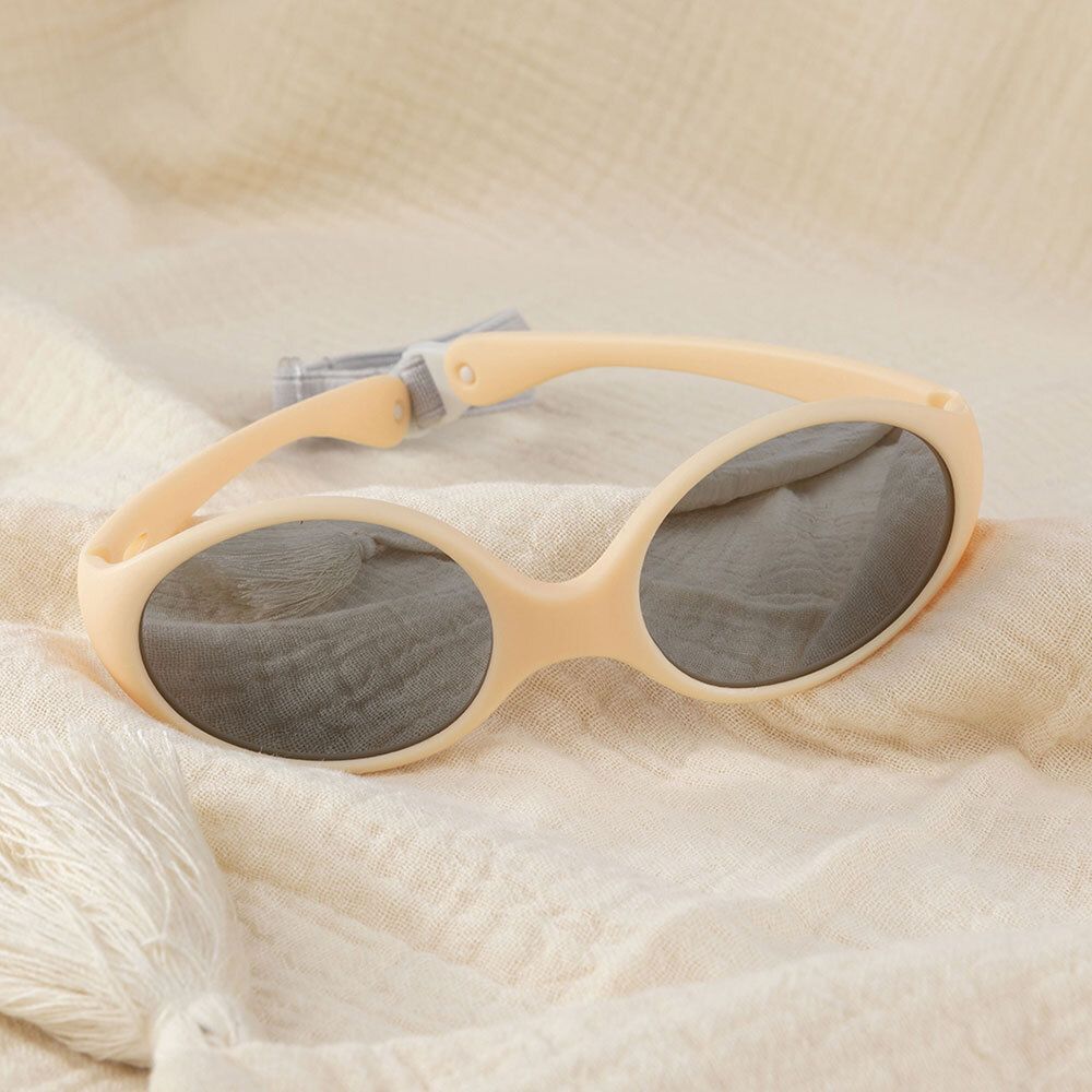 Beige zonnebril met grijze glazen en grijze band. Geplaatst op beige stof.