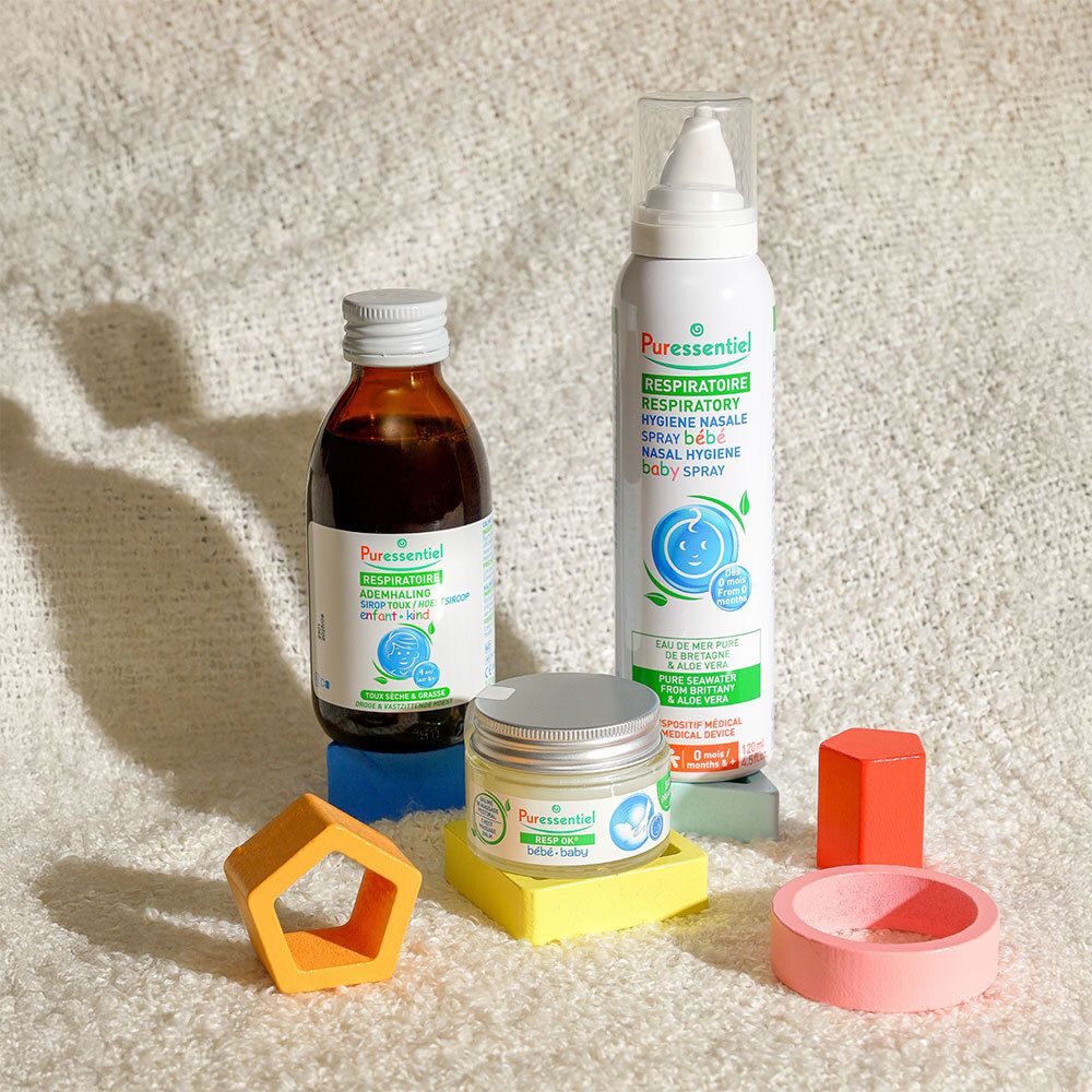 Divers produits de soins pour bébés. Spray nasal, crème, sirop et jouets sur fond blanc.
