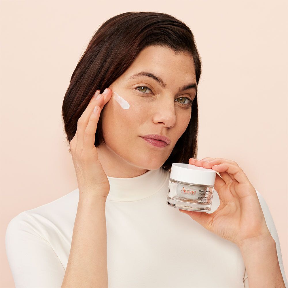 Femme appliquant de la crème. Produit: Avene Hyaluron Activ B3. Pot de crème avec couvercle blanc.