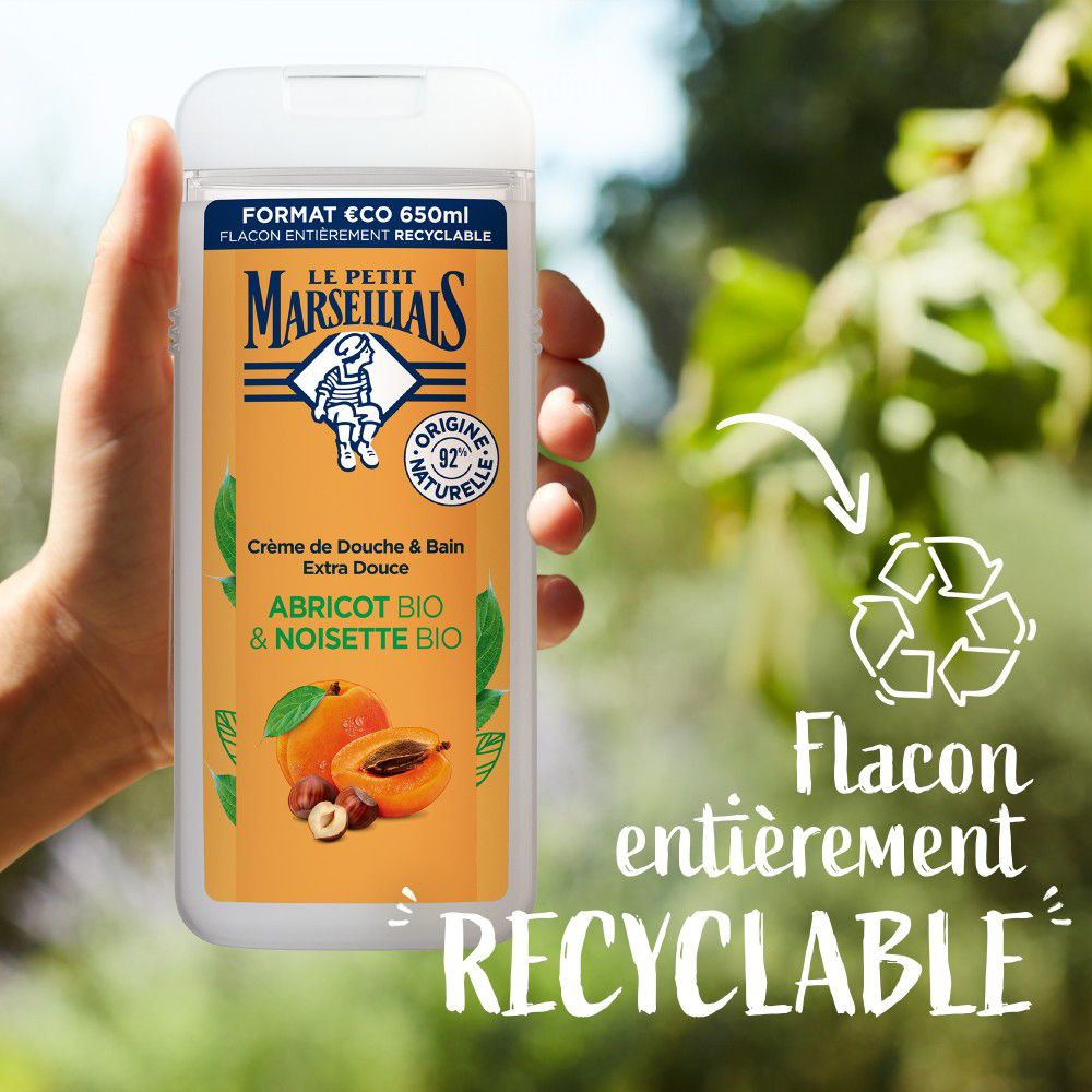 Main tenant un flacon. Texte: Flacon entièrement recyclable. Le Petit Marseillais Crème de Douche & Bain. Abricot BIO & Noisette BIO.
