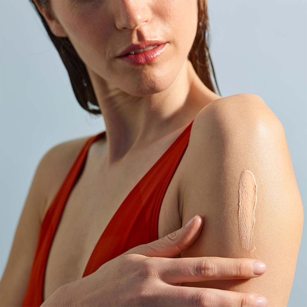 Femme appliquant de la crème sur le bras. Haut rouge. Application de crème.