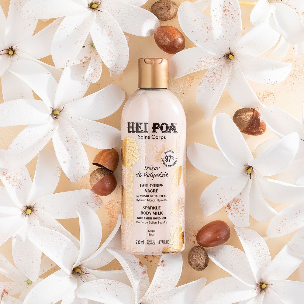 Fles omringd door witte bloemen en noten. Opschrift: Hei Poa, Soins Corps, Trésor de Polynésie, Lait Nacré, Sparkle Body Milk. 97% natuurlijk.