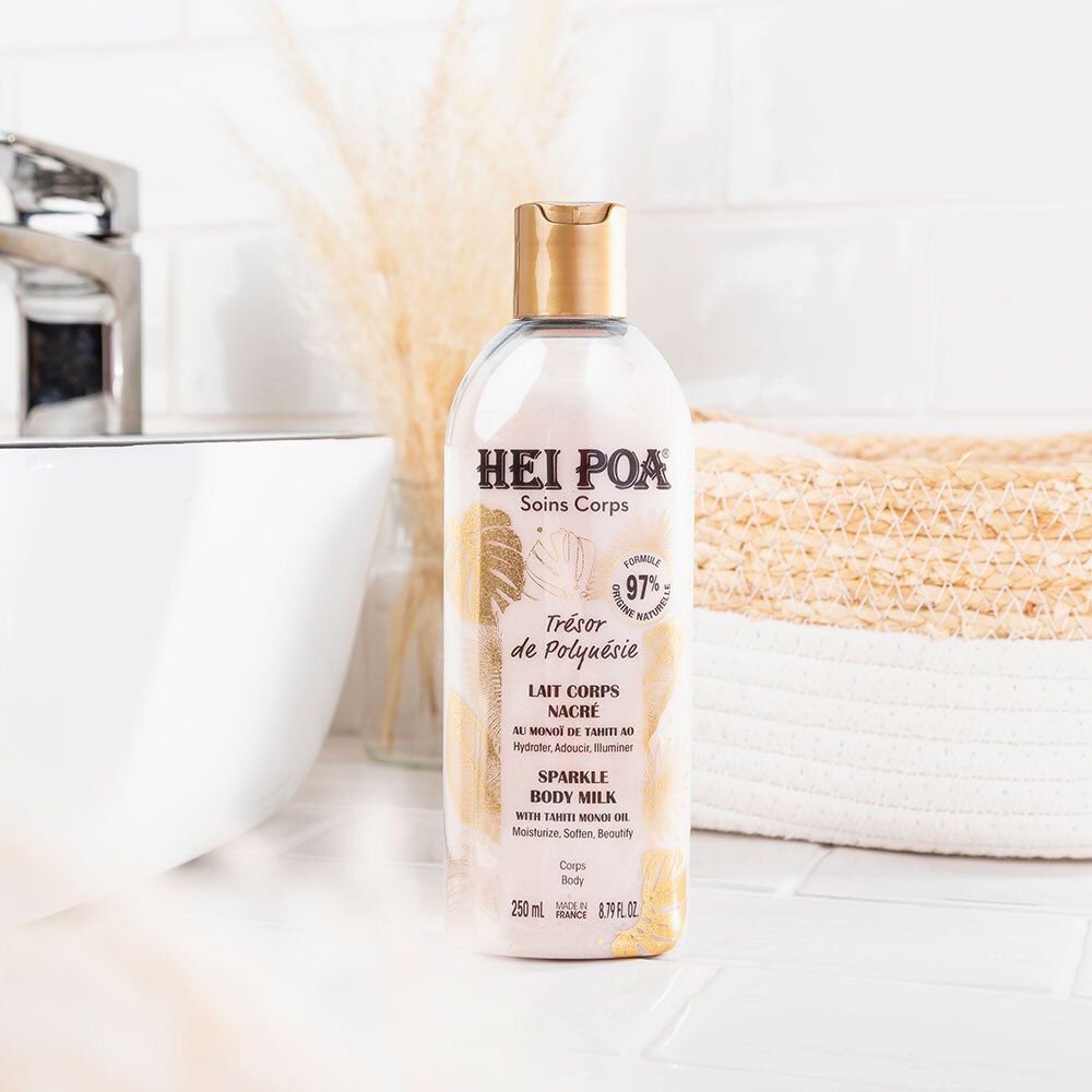 Fles op witte achtergrond met wastafel en mand. Opschrift: Hei Poa, Soins Corps, Trésor de Polynésie, Lait Nacré, Sparkle Body Milk. 97% natuurlijk.
