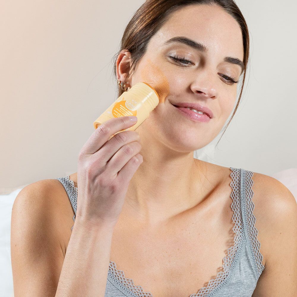 Vrouw brengt een geel masker aan op haar gezicht. Ze houdt het masker vast.