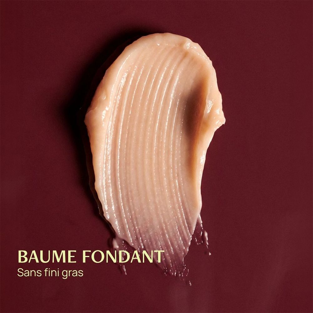Een romige, lichtbeige textuur met ribbels, geplaatst op een donkerrode achtergrond. "BAUME FONDANT Sans fini gras".