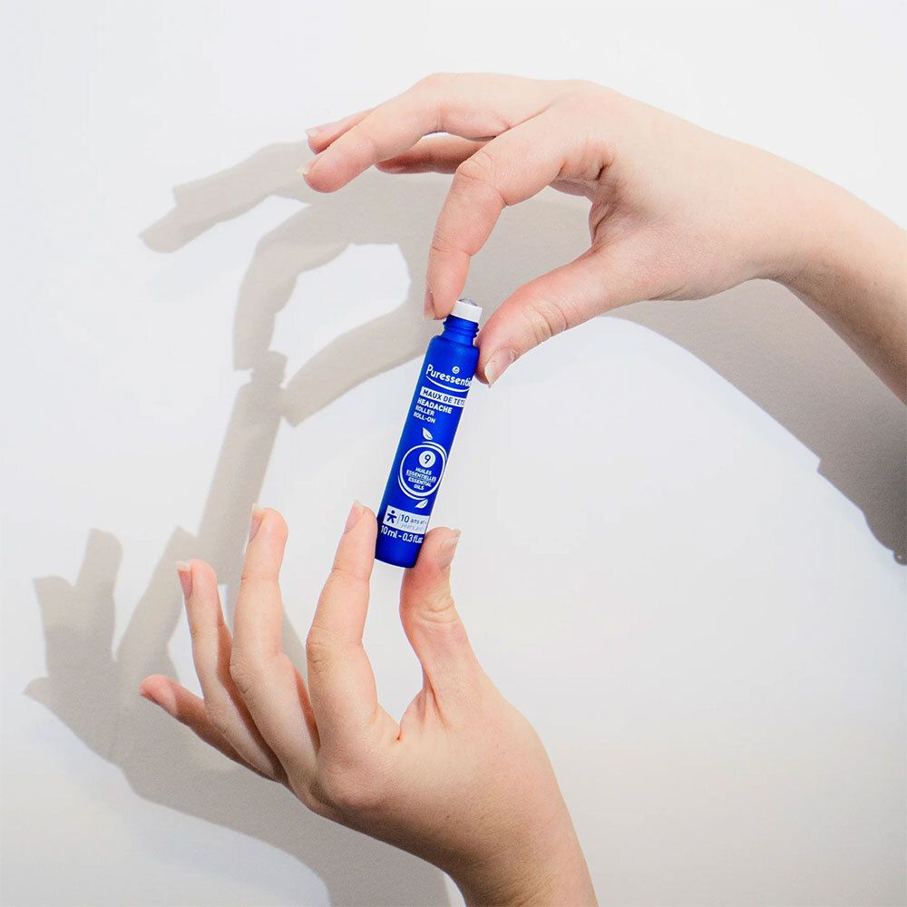 Persoon houdt blauwe roll-on vast. Merk: Puressentiel. Tekst: Maux de tête. Klein product.