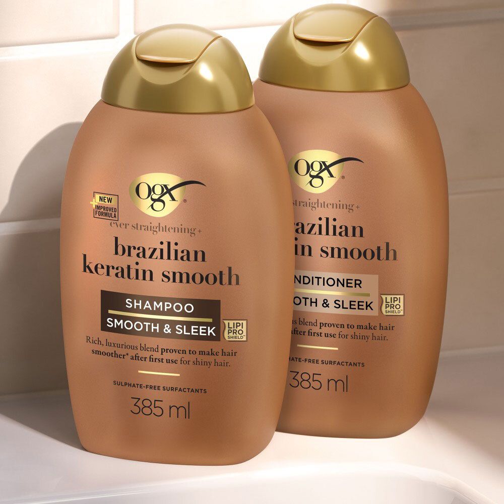 Twee bruine OGX flessen met gouden doppen. Eén is shampoo, de ander conditioner. Beide 385 ml.