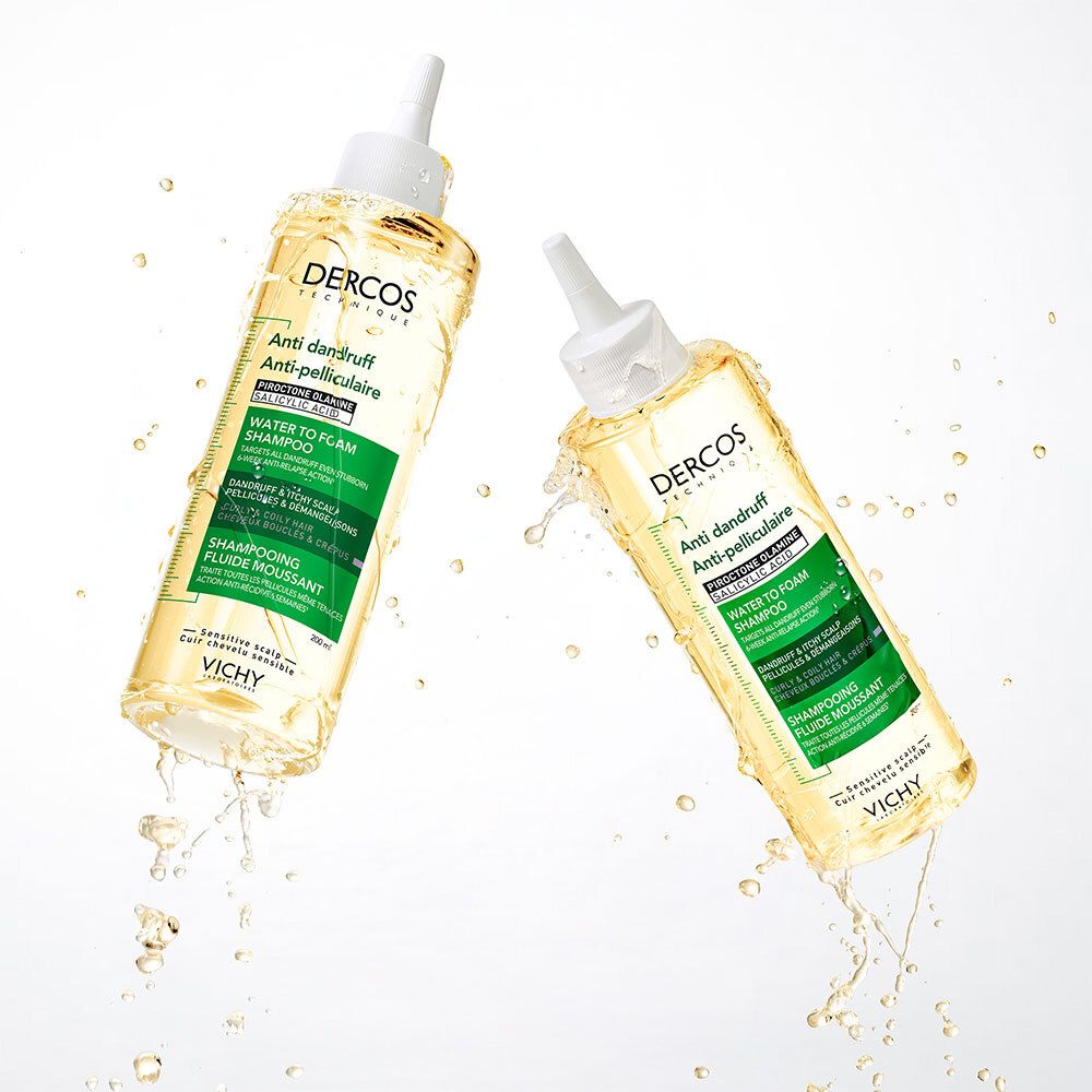 Deux bouteilles de shampoing antipelliculaire Dercos avec logo Vichy, entourées d'éclaboussures d'eau. Liquide jaune, bouchon blanc.