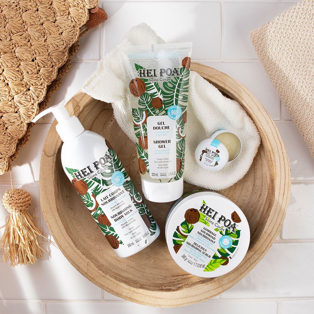 Houten kom met producten: douchegel, body milk, crème. Kokos- en bladerenpatroon. Tekst: HEI POA.