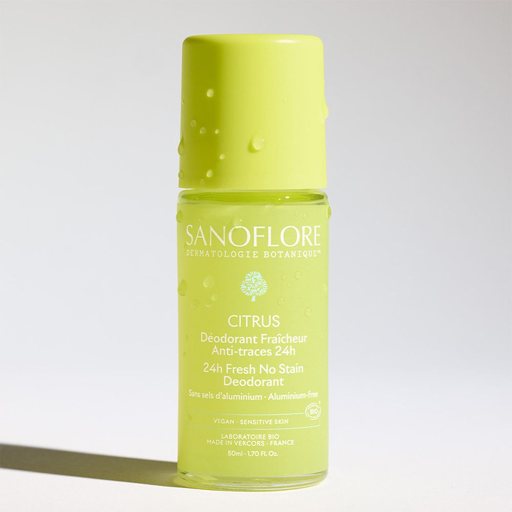 Een roll-on deodorant. Groen-gele fles met dop. Tekst: Sanoflore, Citrus, 24H Fresh No Stain Deodorant. Druppels op de fles.