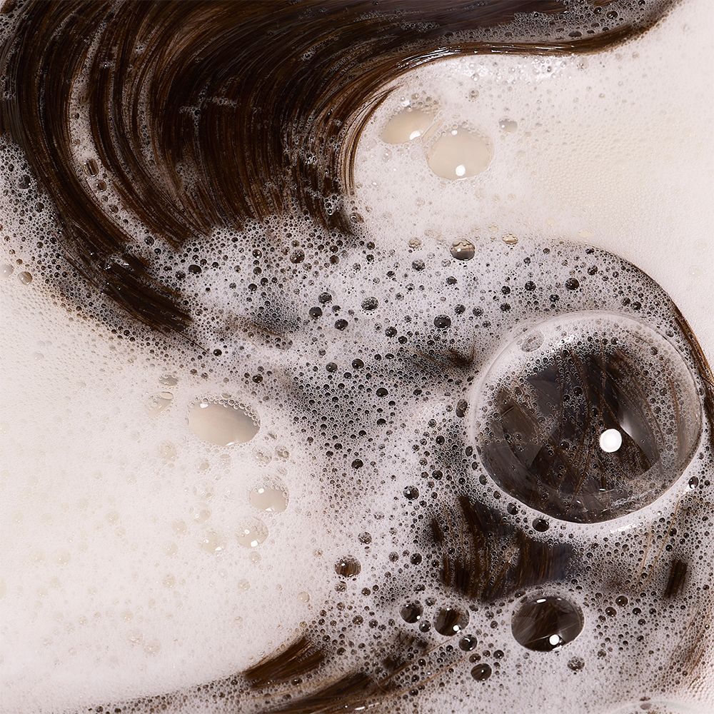 Gros plan sur des cheveux bruns dans de la mousse. Bulles.