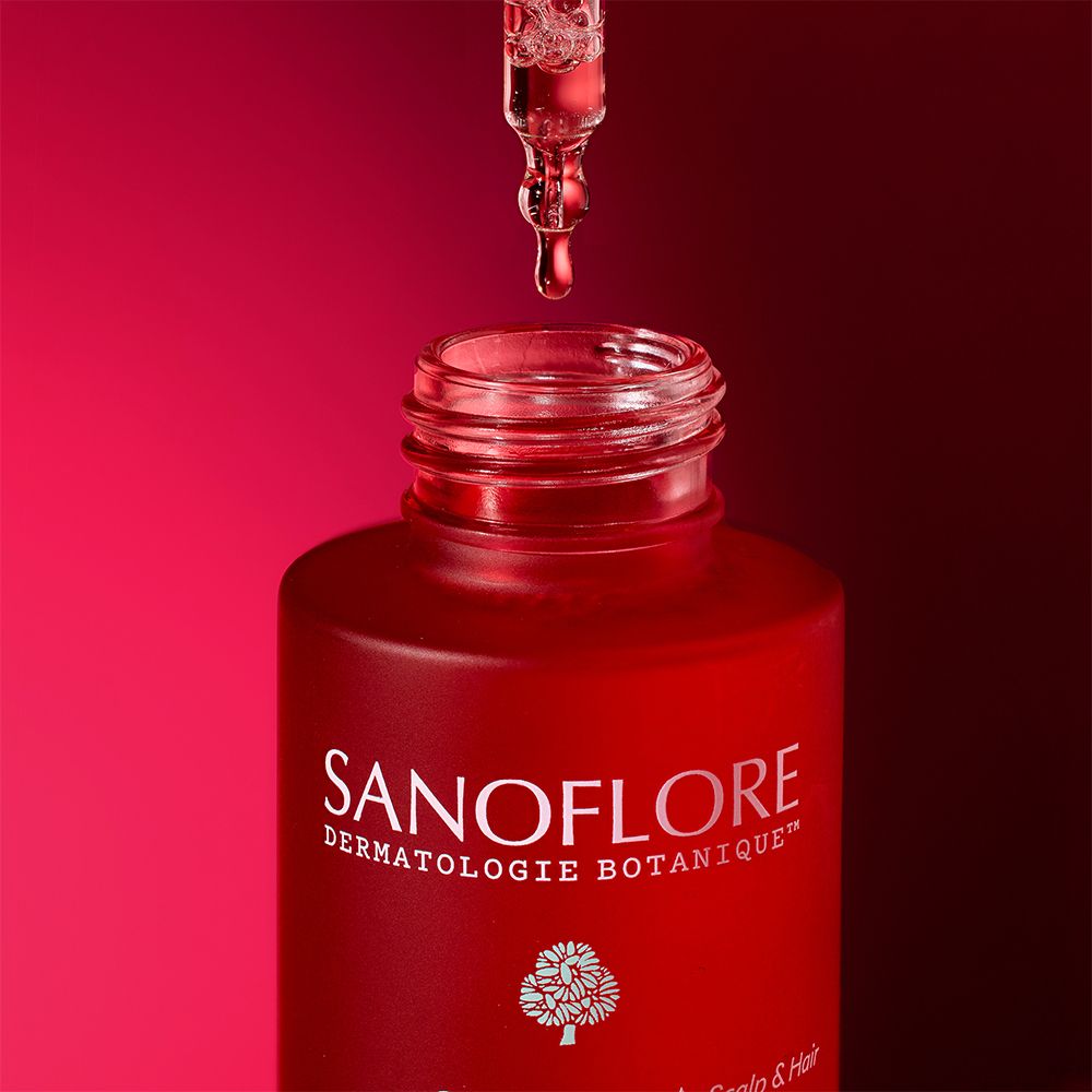 Serum druppelt uit een pipet in een rode fles. Rode achtergrond.