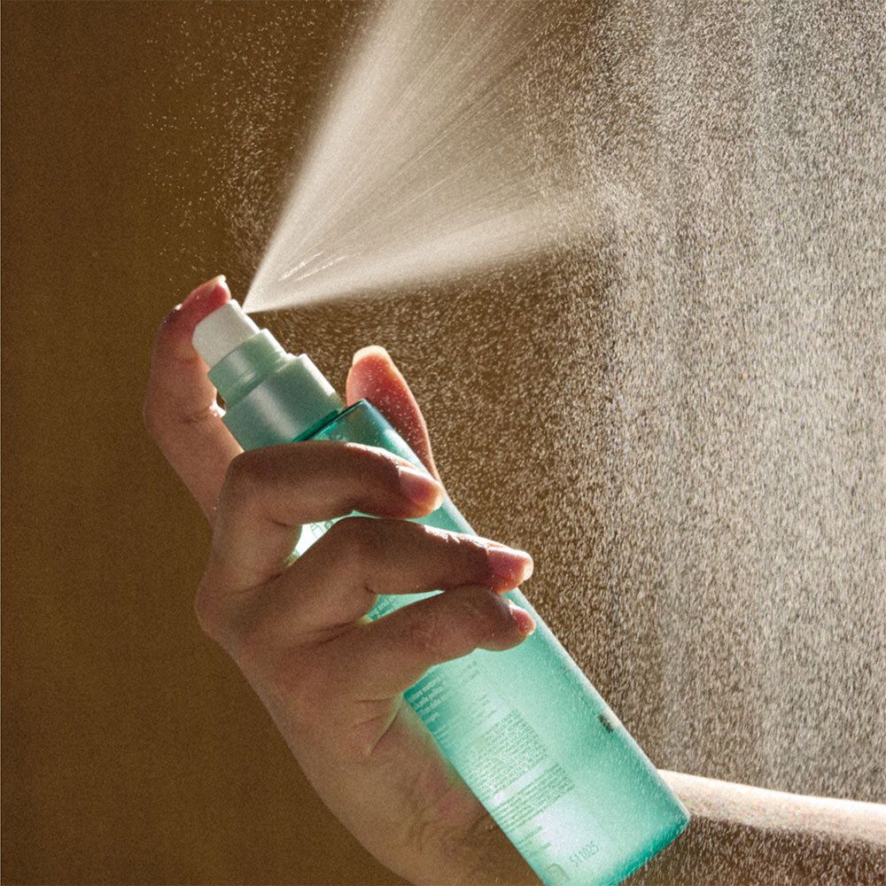Hand houdt groene sprayfles. Sproeimist zichtbaar. Fles met witte sproeikop.