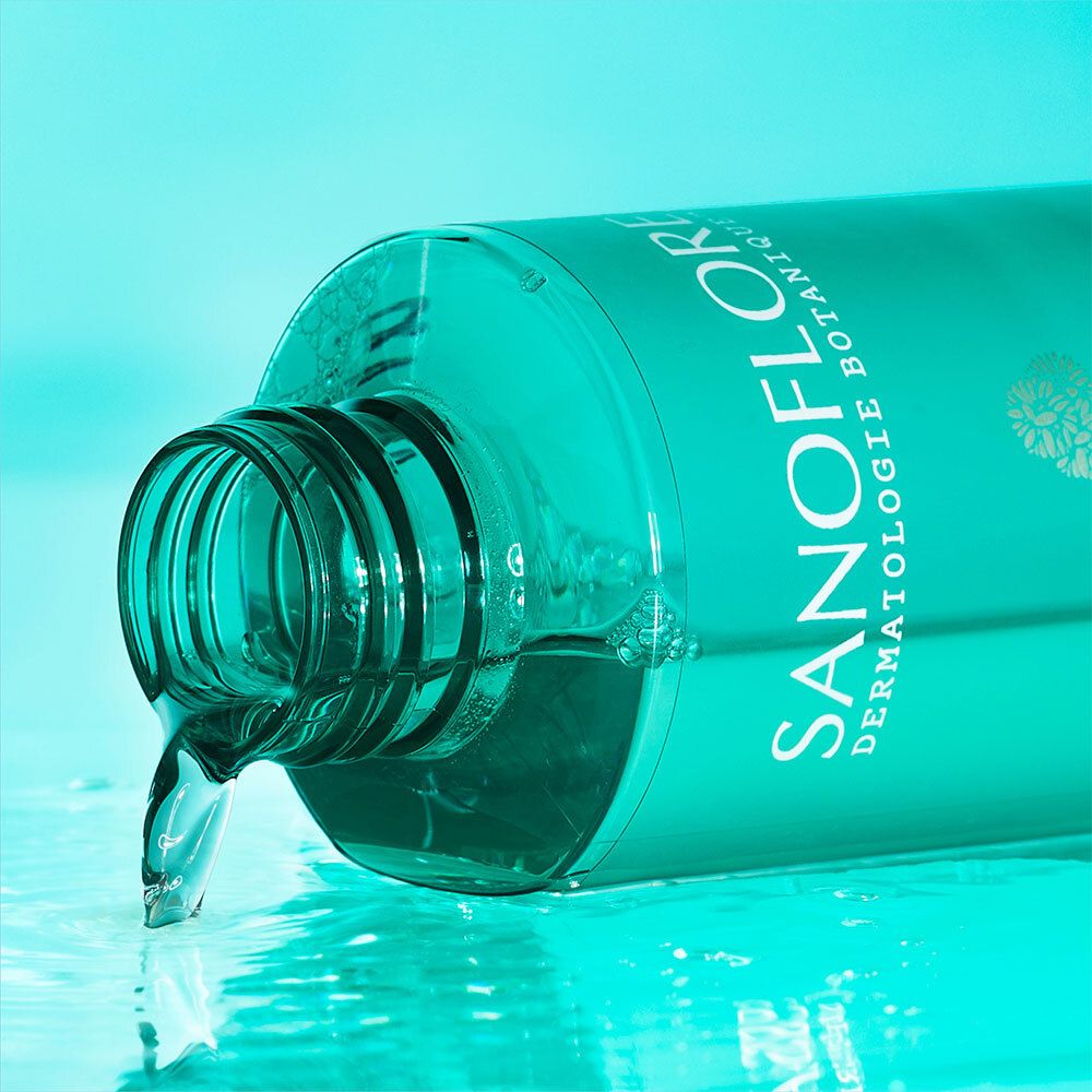 Liquide s'écoulant d'un flacon turquoise. Inscription: Sanoflore Dermatologie Botanique. Flacon couché.