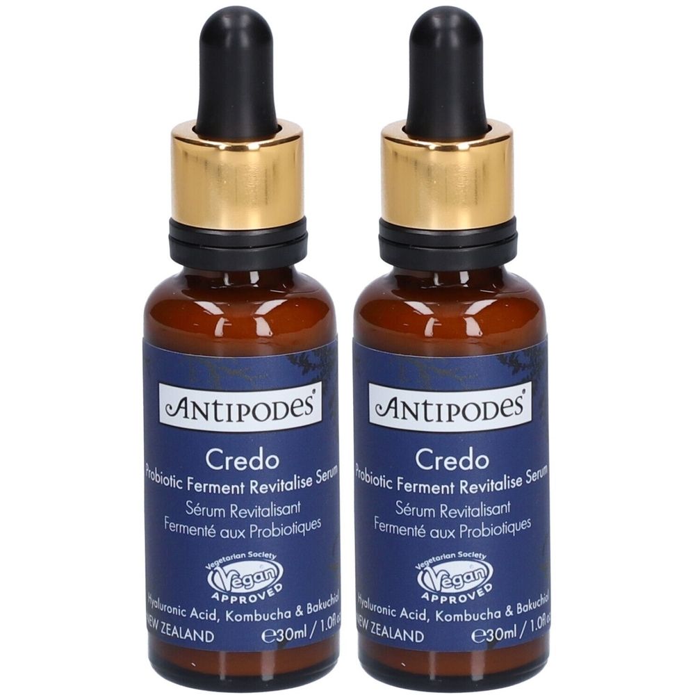 Twee bruine glazen flessen met zwarte pipetten en gouden doppen. Blauwe etiketten met tekst: ANTIPODES Credo Probiotic Serum. Vegan-zegel.