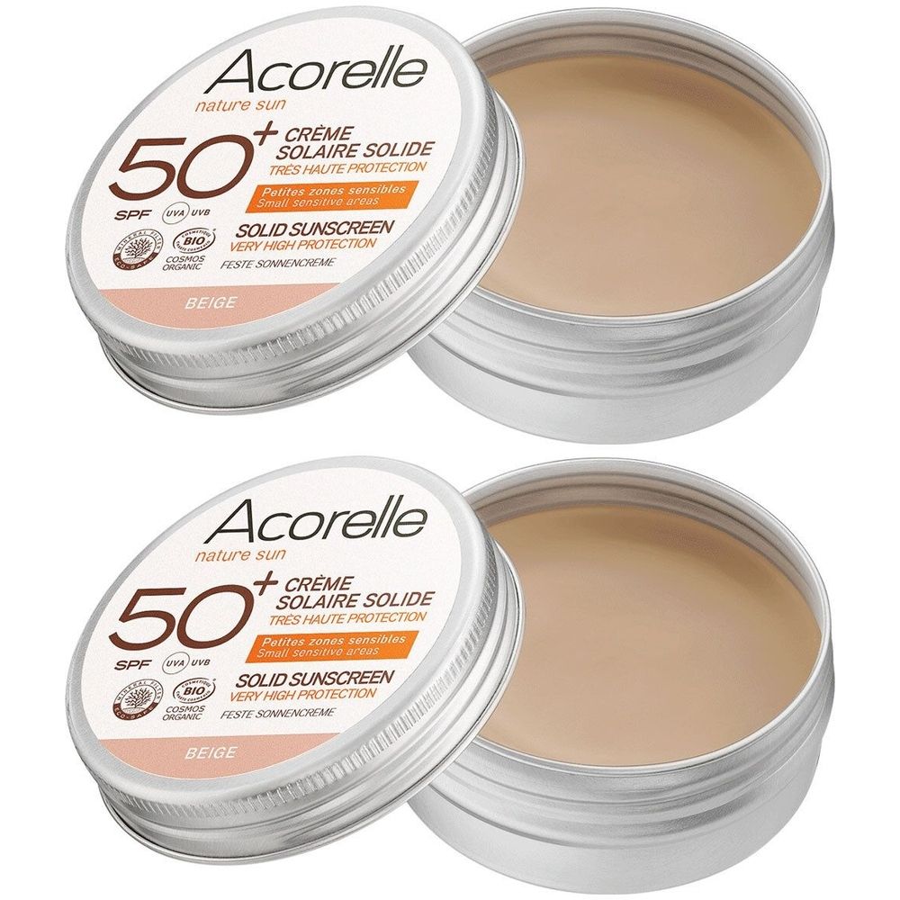 Twee ronde zilverkleurige potjes met beige crème. Deksel met tekst: Acorelle, SPF 50+, Crème Solaire Solide, Beige.