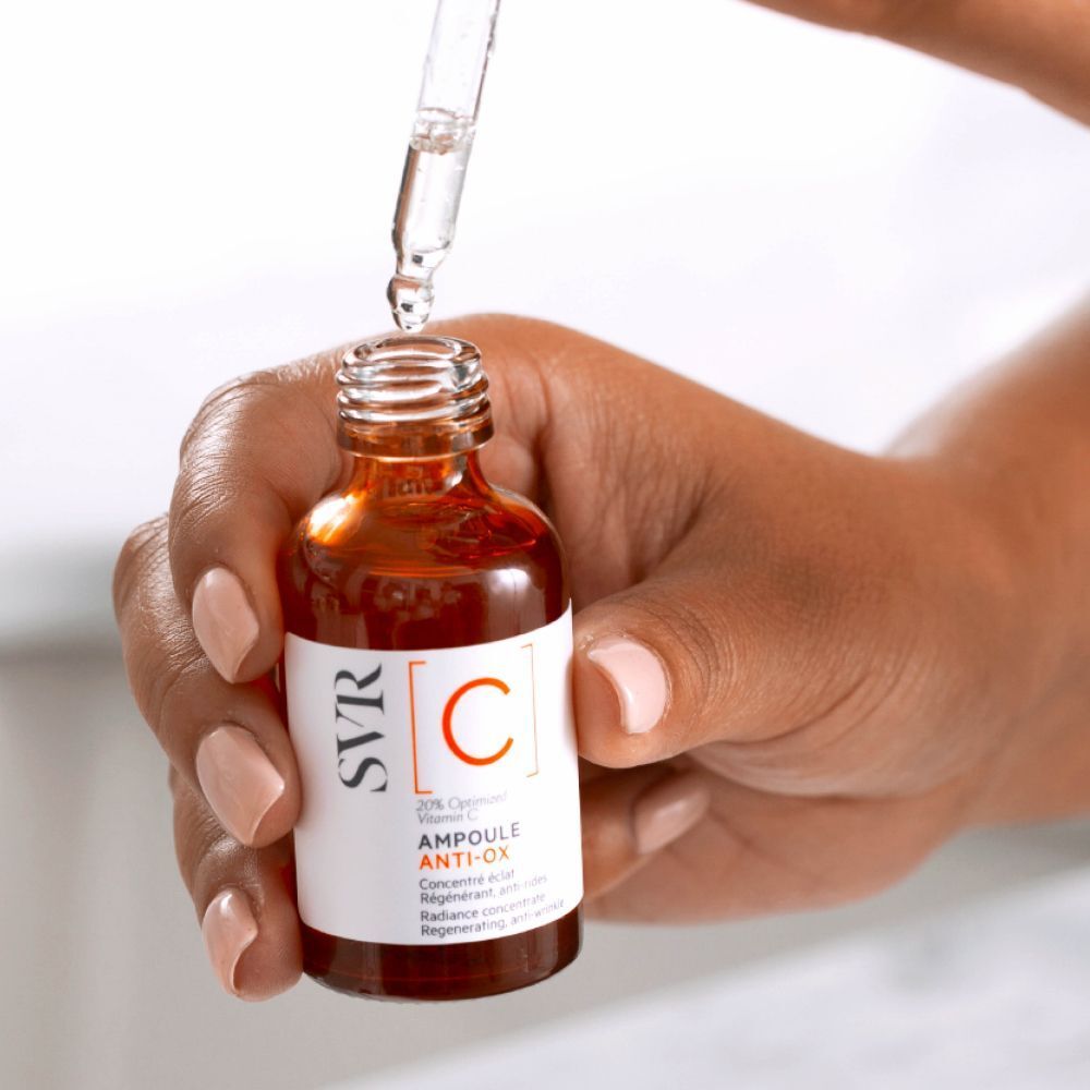 Hand houdt flesje met druppelaar. Druppels vallen. Etiket: SVR [C] Ampoule Anti-Ox.