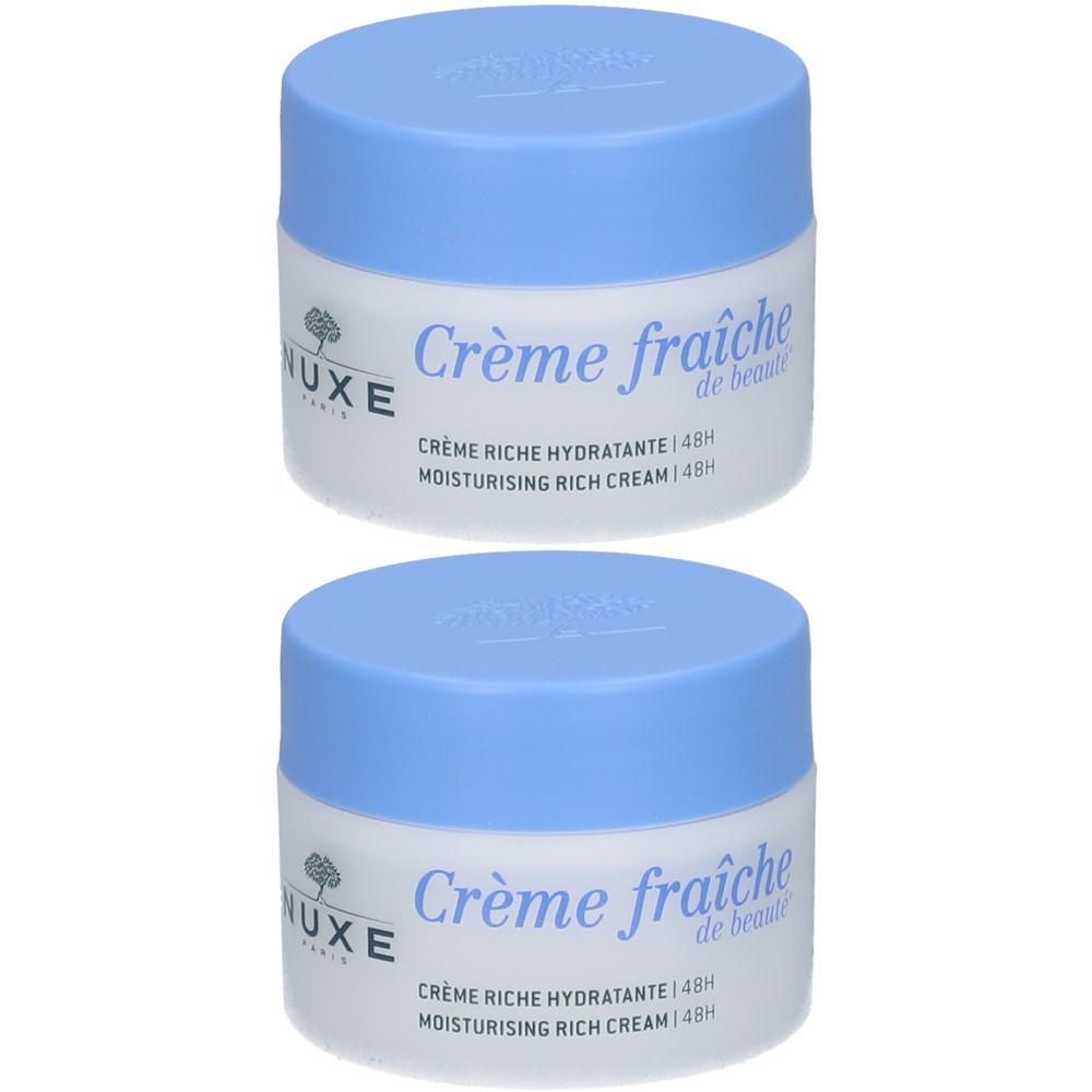 Deux pots de crème Nuxe Crème fraîche de beauté. Pots blancs avec couvercles bleu clair. Inscription : Crème fraîche de beauté, Crème Riche Hydratante 48H.