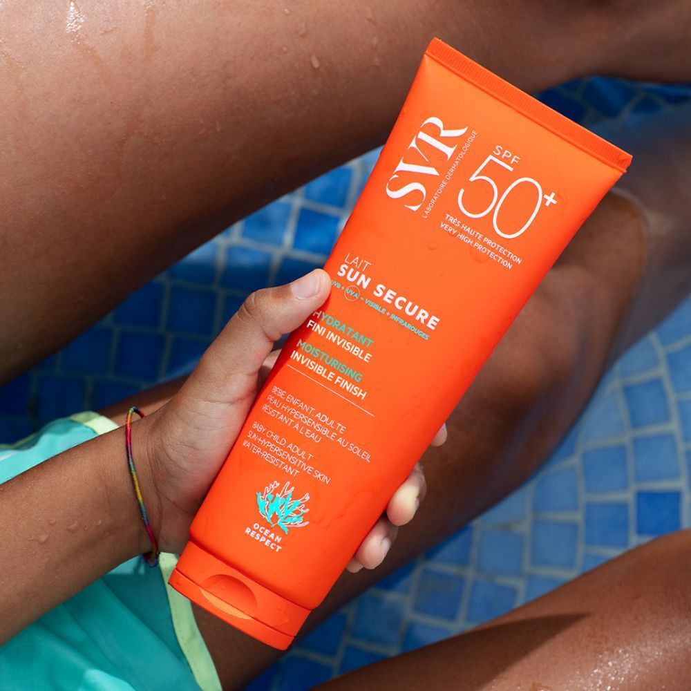 Persoon houdt een tube SVR SUN SECRUE Melk SPF 50+ vast. Oranje tube met witte tekst. Tekst: Lait Sun Secure, Fini Invisible, Moisturising.
