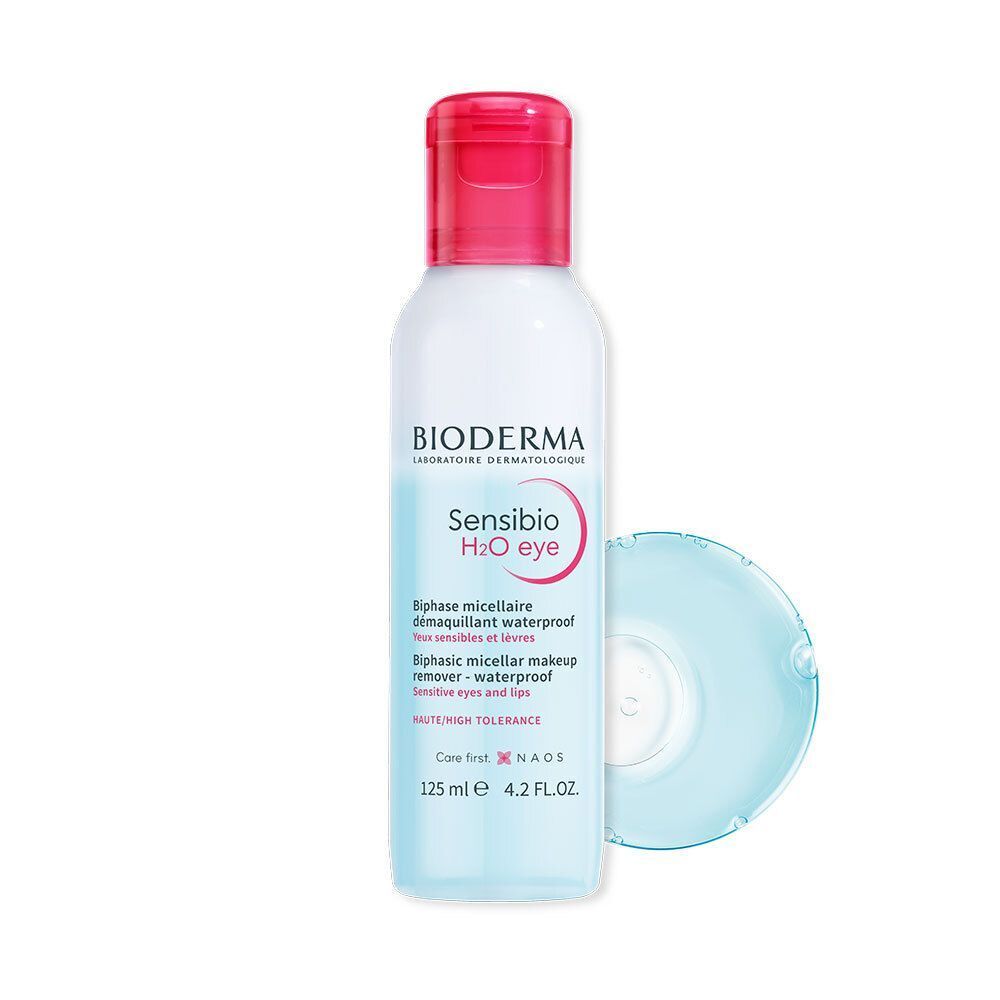 Un flacon de Bioderma Sensibio H2O eye avec bouchon rose et un coton bleu. Inscription Sensibio H2O eye et Biphase micellaire démaquillant waterproof.