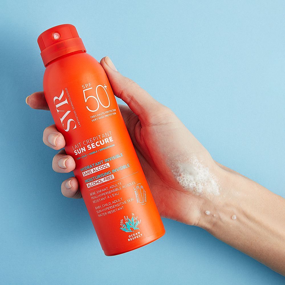 Een hand houdt een oranje spray. Opschrift: SVR, SPF 50+, SUN SECURE, hydraterend onzichtbaar, alcoholvrij.