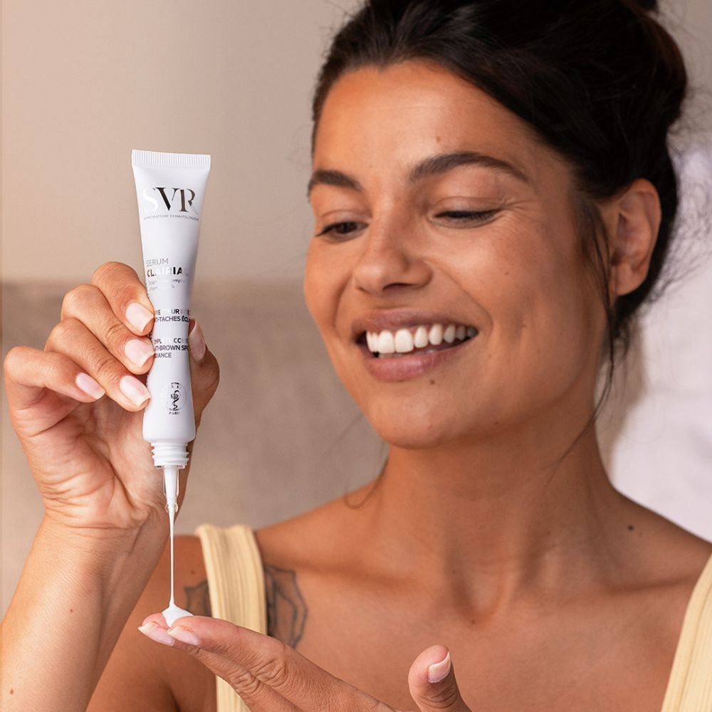 Vrouw met SVR Clairial Serum. Tube wordt op de hand aangebracht. Lachende gezichtsuitdrukking. Gele top.
