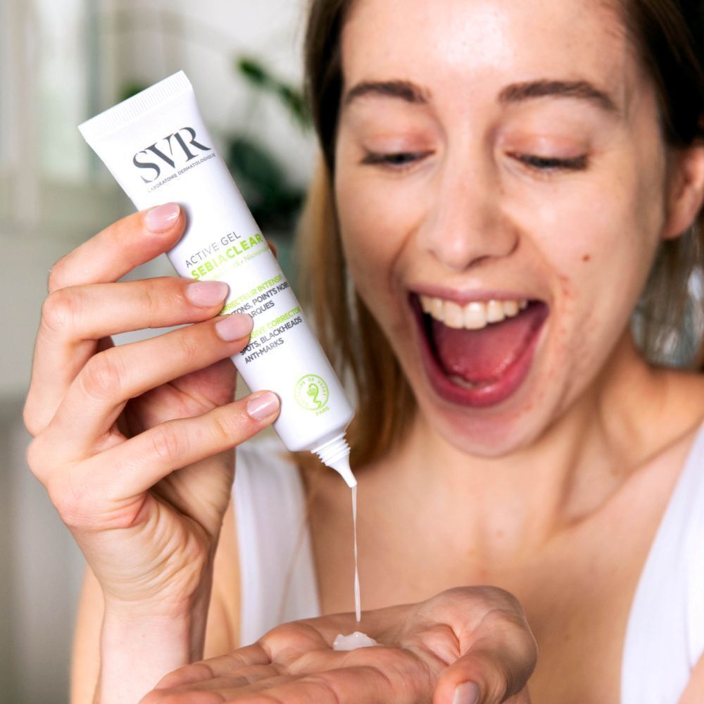 Een vrouw houdt een tube SVR SEBIACLEAR Active Gel vast. Product wordt op de hand gedrukt. Vrouw lacht.