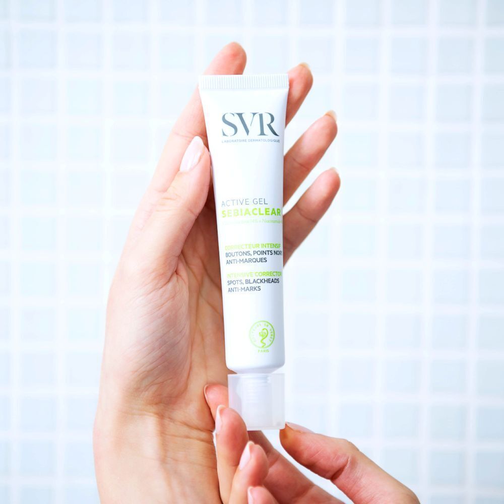 Een hand houdt een tube SVR SEBIACLEAR Active Gel vast. Witte tube met groene en zwarte tekst. SVR-logo.