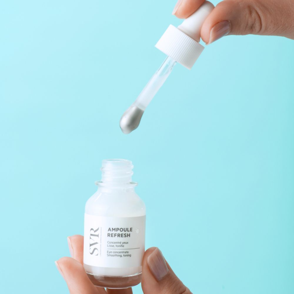 Een flesje met witte dop en etiket. Opschrift: SVR, Ampoule Refresh, Eye concentrate. Pipet wordt vastgehouden.