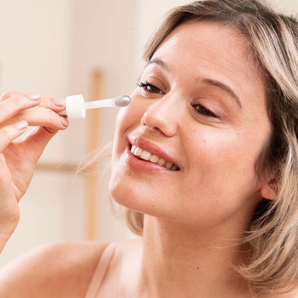 Vrouw houdt een pipet voor het oog. Geen producten zichtbaar.