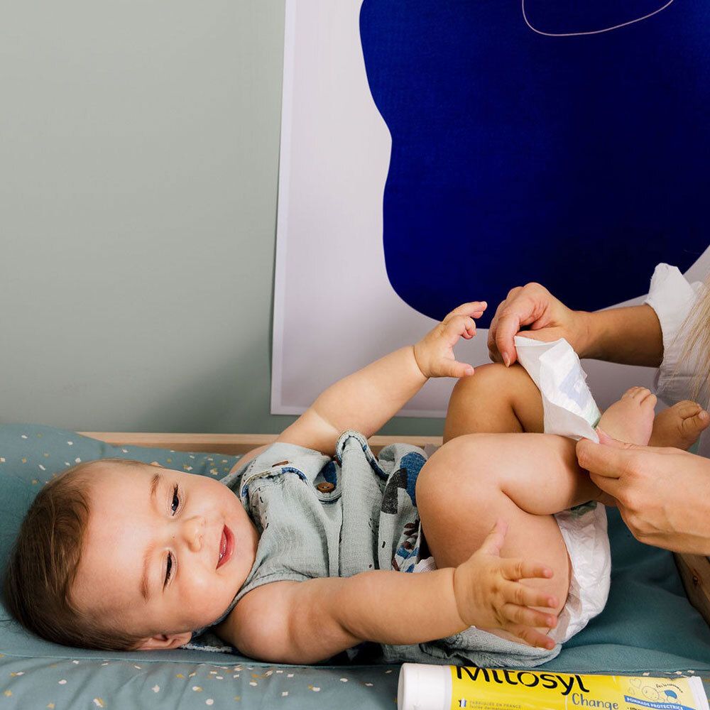 Baby wordt verschoond. In beeld: Mitosyl Change tube. Tekst: Dès la naissance, Pommade Protectrice.