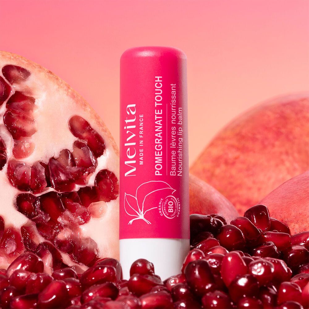 Roze lippenbalsemstift met Melvita-logo, granaatappelmotief en biologisch label. Omringd door granaatappelvruchten en -zaden.