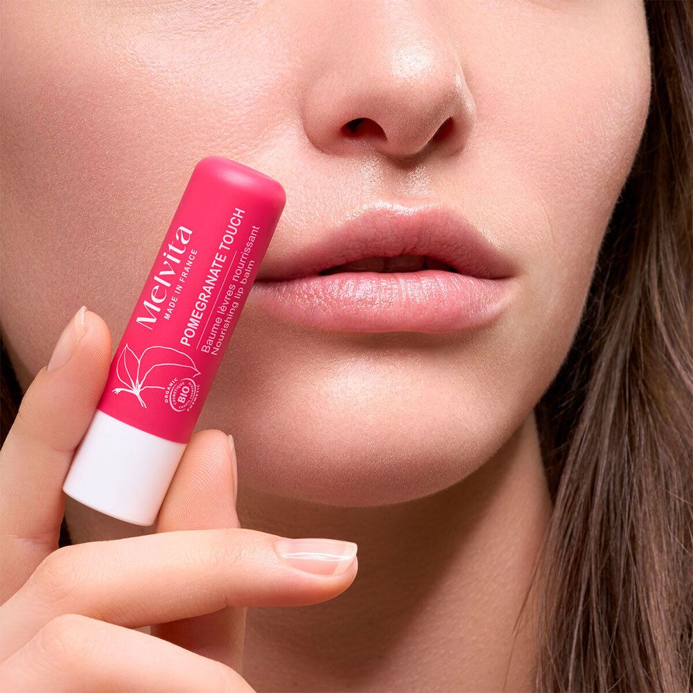 Persoon houdt roze lippenbalsemstift voor lippen. Op de stift staat: Pomegranate Touch, Melvita, biologisch label.