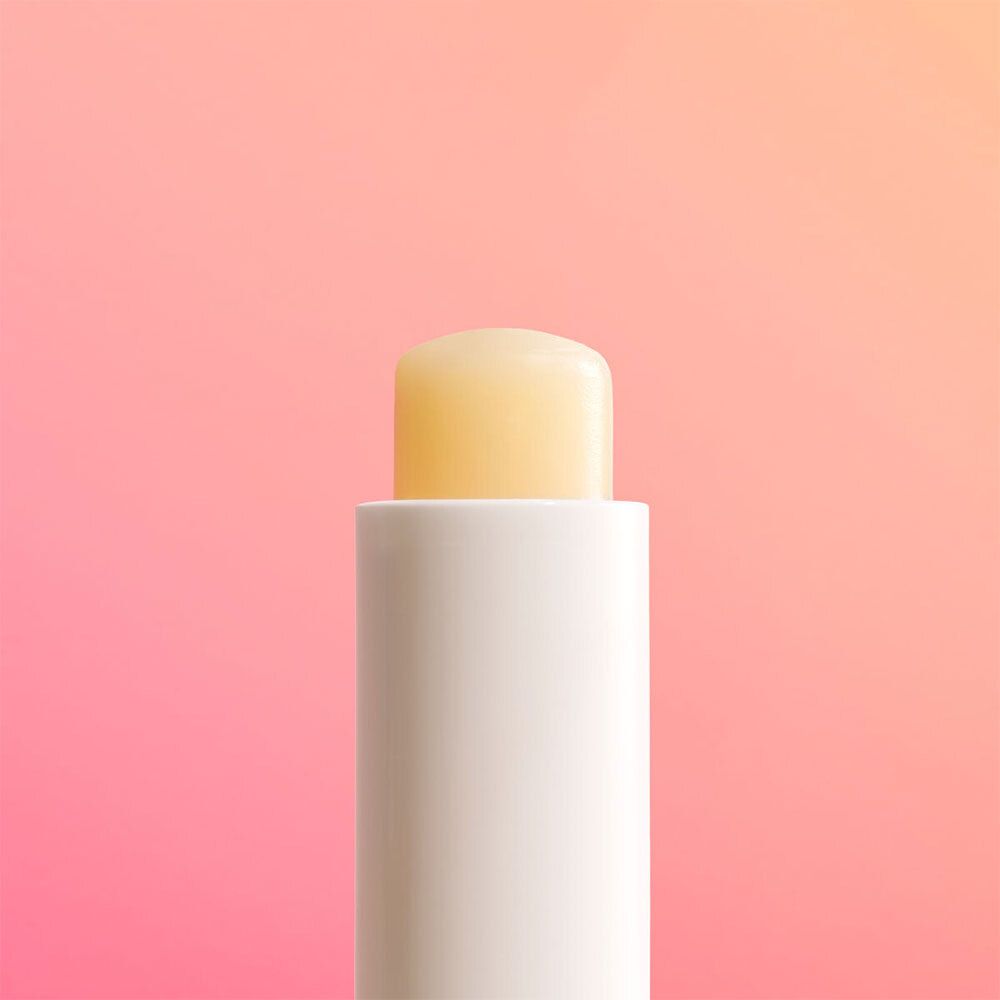 Close-up van een witte lippenbalsemstift met gele balsem. De stift staat op een roze achtergrond.