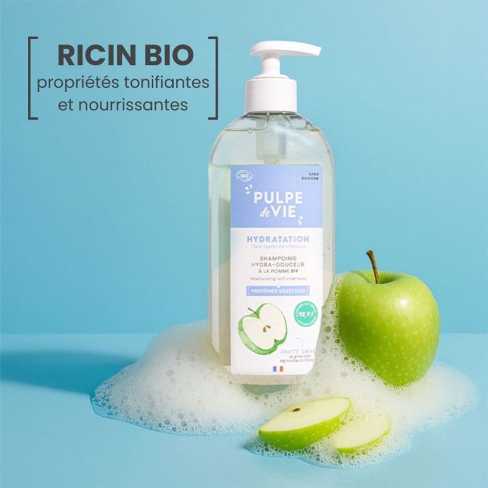 Un flacon de shampoing transparent avec texte et illustration de pomme. Pomme verte et mousse à côté. Certification bio.