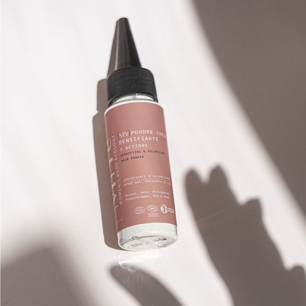 Flacon avec étiquette rose contenant de la poudre pour cheveux. Embout applicateur noir.