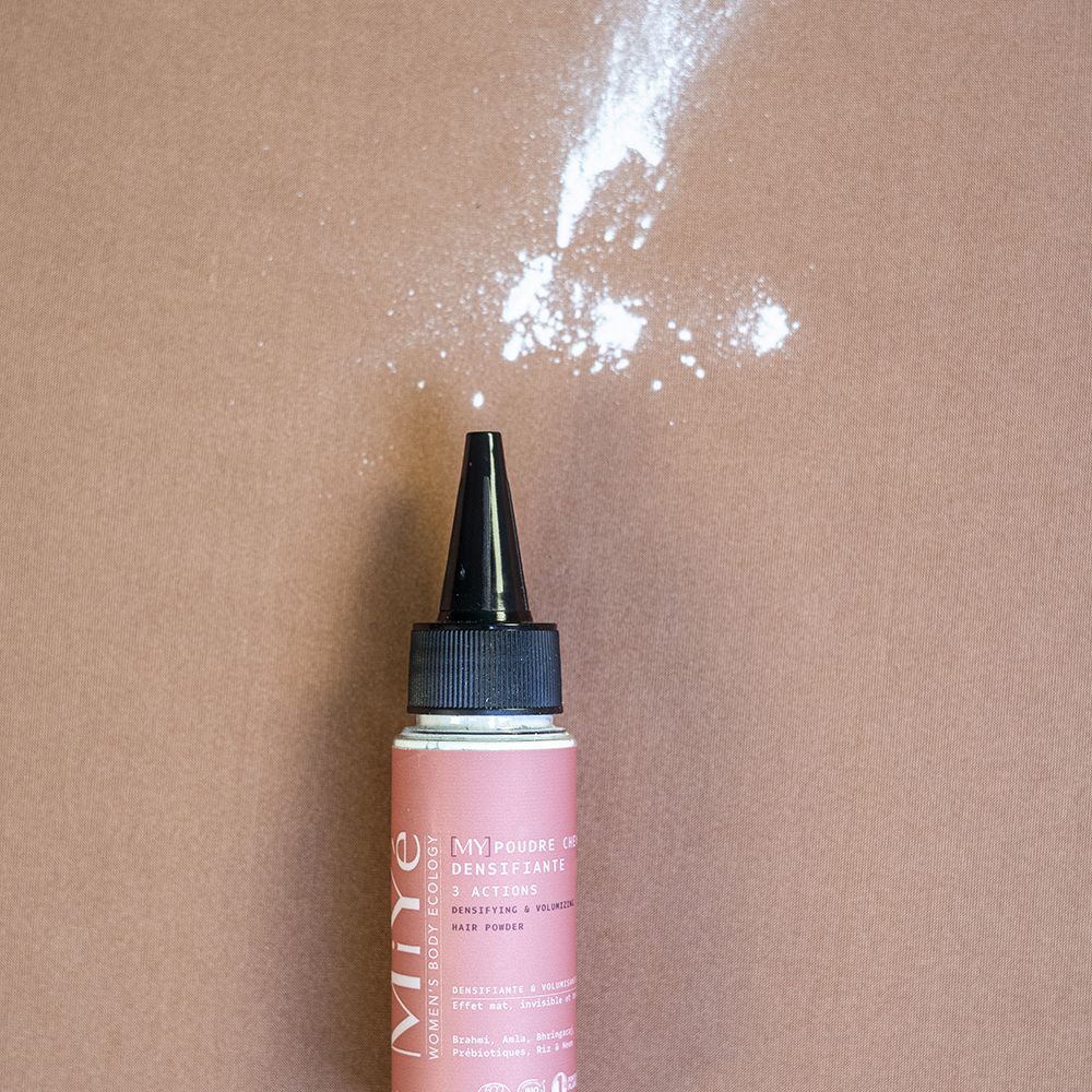 Une bouteille rose avec un applicateur noir, d'où sort une poudre blanche.