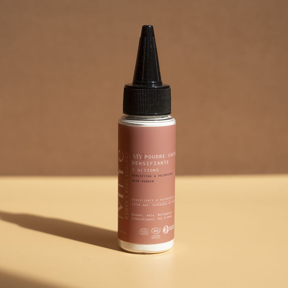 Flacon à étiquette brune et applicateur noir, contenant de la poudre densifiante pour cheveux.