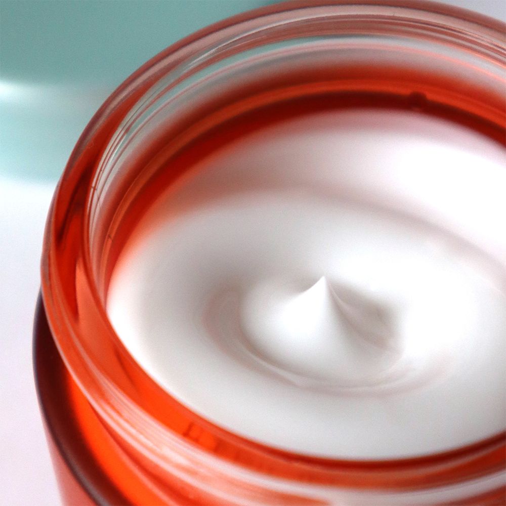 Gros plan d'un pot rouge avec crème blanche. Crème avec pointe au centre.