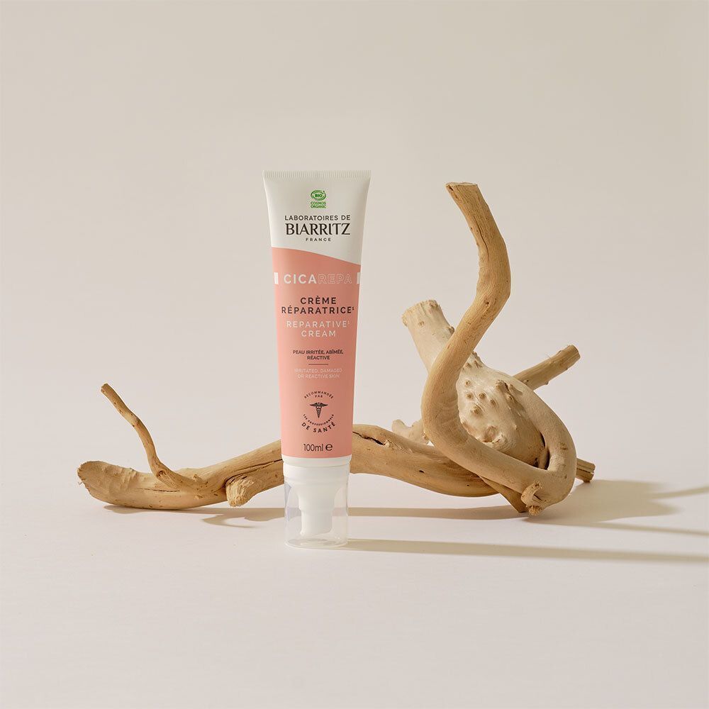 Roze-witte crème tube met tekst. Opschrift: CICA REPA, Crème Réparatrice. Handen brengen de crème aan op een litteken.