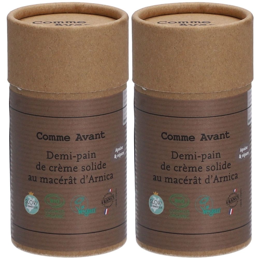 Twee cilindrische containers van bruin karton. Opschrift: Comme Avant, Demi-pain de crème solide au macérât d'Arnica. Met Vegan- en Slow Cosmétique-labels.