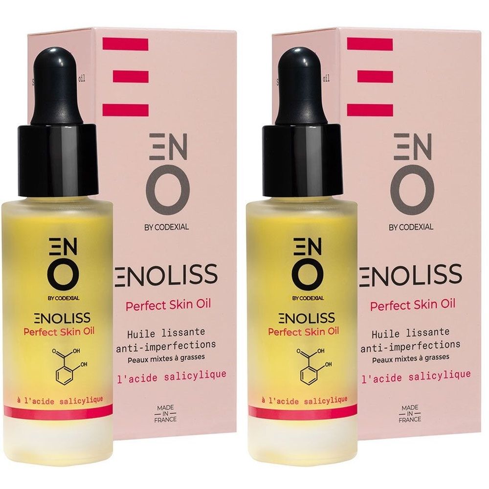 Twee flessen gele olie met zwarte dop en etiket. Opschrift: ENO Enoliss Perfect Skin Oil. Roze verpakking op de achtergrond.