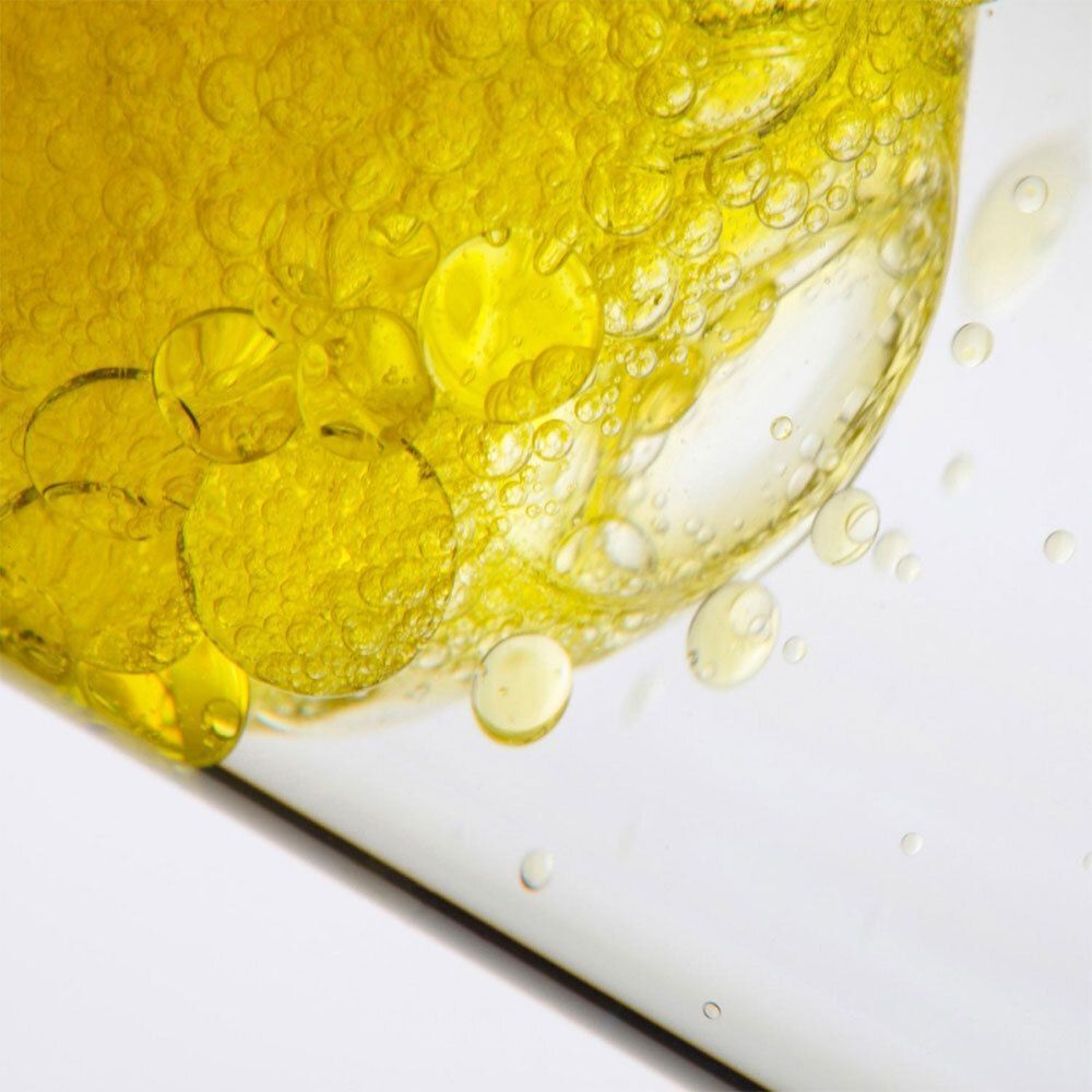 Close-up van gele vloeistofdruppels en bellen. Vloeistof in een transparante glazen fles.