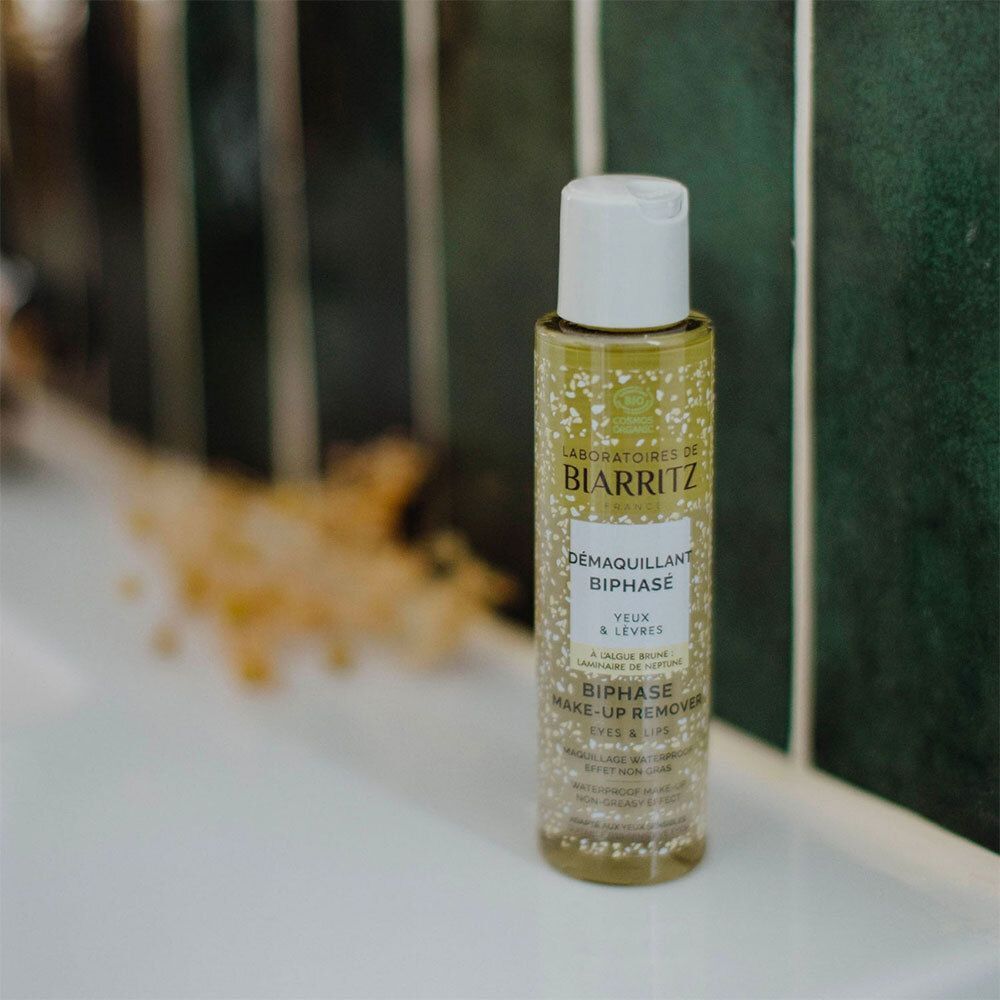 Fles Démaquillant Biphasé Yeux & Lèvres Bio op een wit oppervlak. Groene achtergrond.