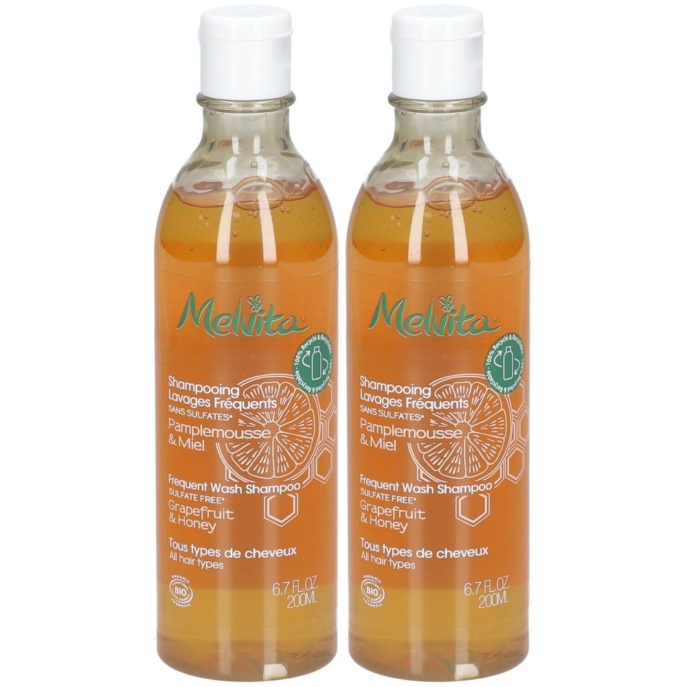 Twee flessen Melvita shampoo. Transparante flessen met witte doppen. Etiketten met productinfo en logo. Grapefruit en honing.