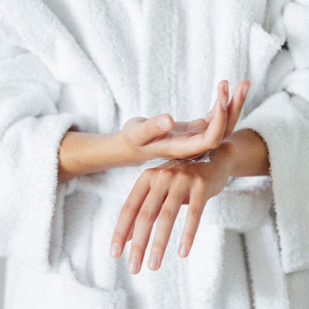Personne appliquant de la crème sur les mains. Peignoir blanc. Gros plan sur les mains.