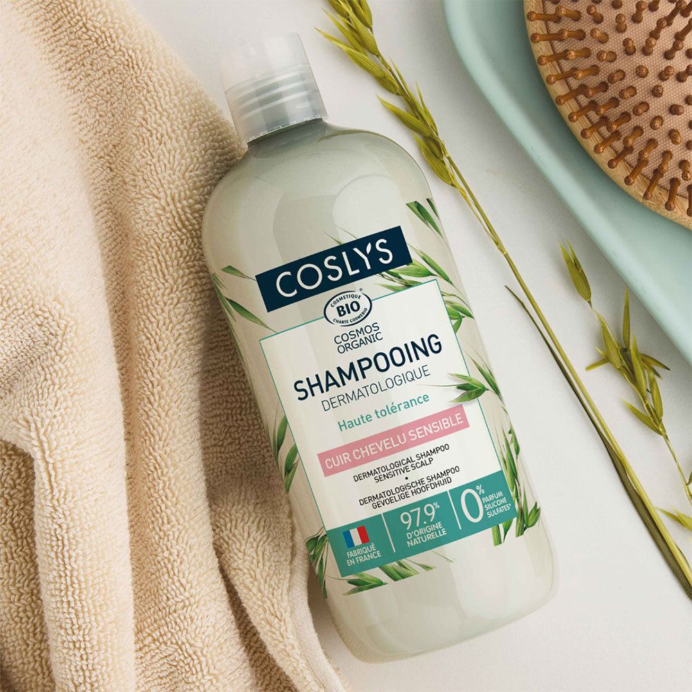Flacon de Coslys Shampooing dermatologique sur une serviette. Inscription: Cosmos Organic, Shampooing, dermatologique, haute tolérance. Avec brosse.